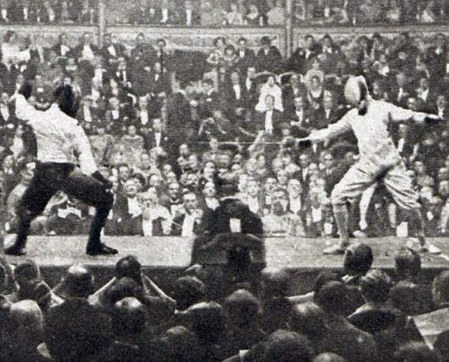 Zwei Männer fechten in einem Stadion, einer mit einem Schwert und der andere mit einem Schild, während eine Menge zusieht.