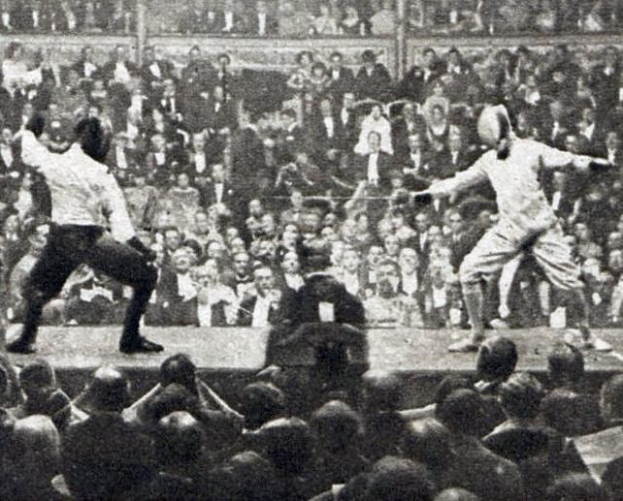 Zwei Männer fechten in einem Stadion, einer mit einem Schwert und der andere mit einem Schild, während eine Menge zusieht.