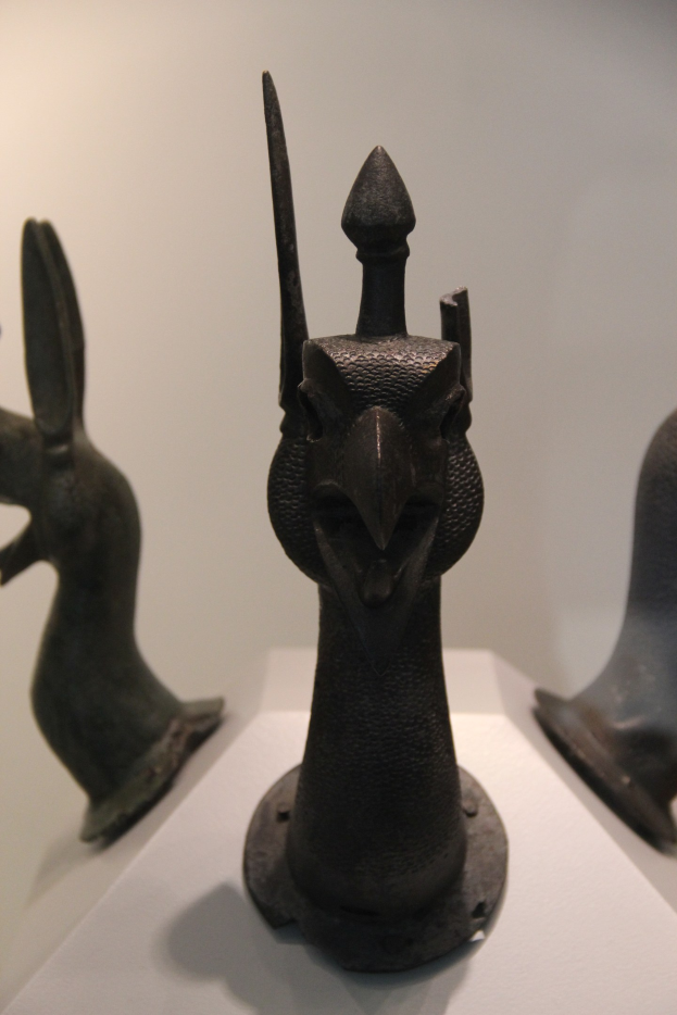 Drei Bronzestatuen in einem Museum ausgestellt, auf einer weißen Oberfläche mit einer Wand im Hintergrund.