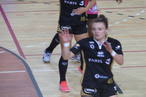 Eine Gruppe von Frauen in Sportkleidung und -schuhen beim Volleyballspielen auf einem Platz.