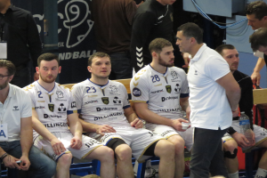 Eine Gruppe von Männern sitzt auf einer Bank, einige halten Flaschen, mit einem Banner im Hintergrund mit der Aufschrift 'Nordkraque vs Bordeaux.'