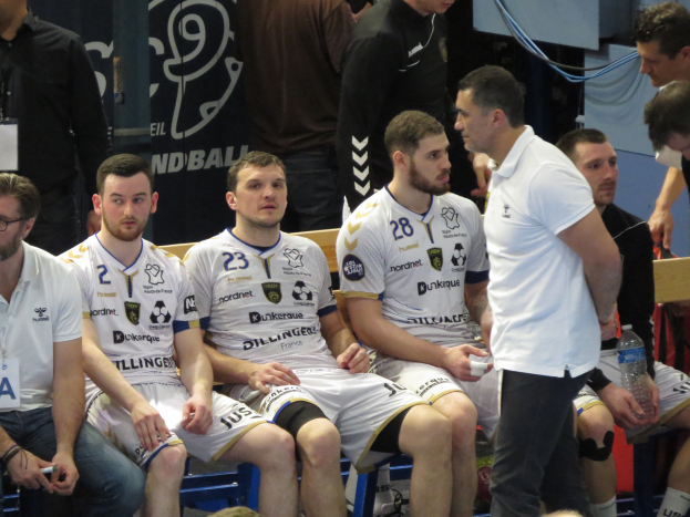 Eine Gruppe von Männern sitzt auf einer Bank, einige halten Flaschen, mit einem Banner im Hintergrund mit der Aufschrift 'Nordkraque vs Bordeaux.'