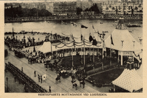 Ein altes Schwarz-Weiß-Foto einer Menge, die sich um einen Karneval mit Zelten, Fahnen, Masten und Pferden im Vordergrund und Gebäuden, Bäumen und Wasser im Hintergrund versammelt hat, mit Text am unteren Rand des Bildes.