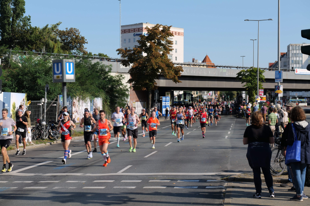 Gruppe von Läufern bei einem Marathon auf einer von Bäumen gesäumten Straße unter einem klaren blauen Himmel.