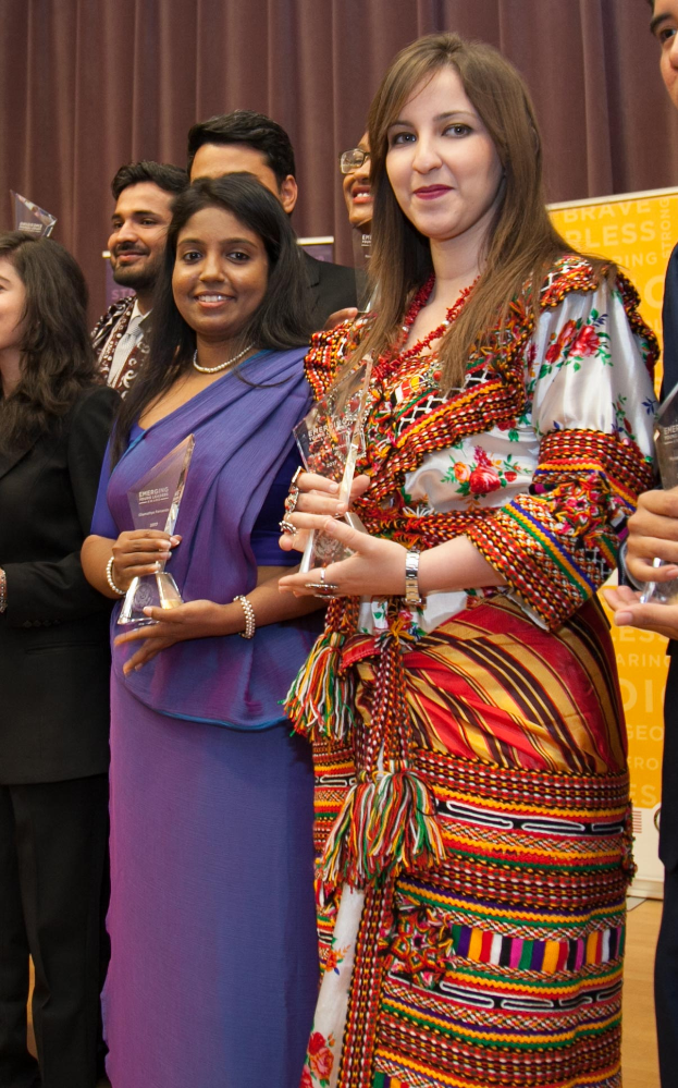Eine Gruppe von Menschen auf einer Bühne mit einer Frau in der Mitte, die eine Trophäe hält, hinter einem Vorhang mit einer Tafel, auf der "Bravo-Blessing-Award-Gewinner" steht.