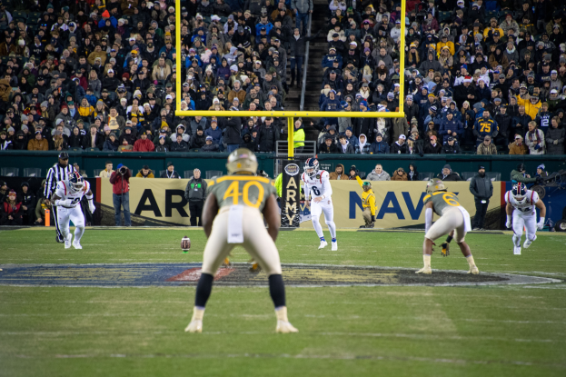 Fußballspieler in Sportkleidung und Helmen konkurrieren auf einem Feld mit Zuschauern auf den Tribünen und sichtbaren Stadionwerbung.