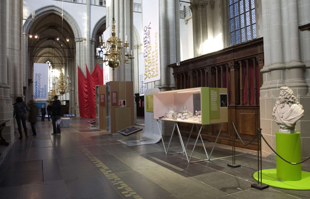 Ein großer Museumsraum mit verschiedenen Artefakten, darunter eine Statue auf einem Sockel, Absperrbaken, Textbanner, Säulen und Kronleuchter sowie einige Besucher.