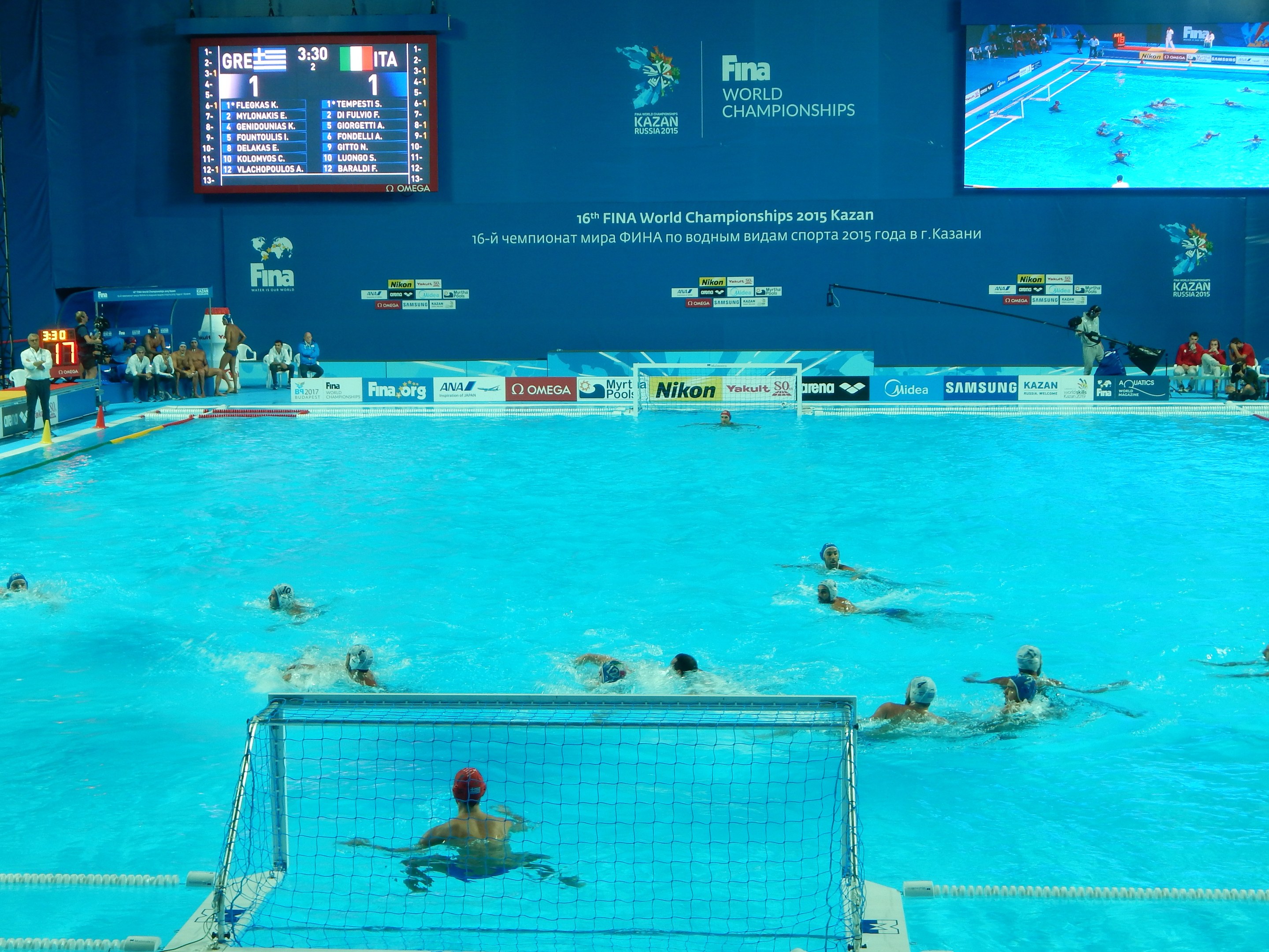 Wasserballspieler bei den FINA-Weltmeisterschaften 2016 in Kazan im Pool gegeneinander antretend, mit Zuschauern auf der linken Seite und einem Scoreboard im Hintergrund.