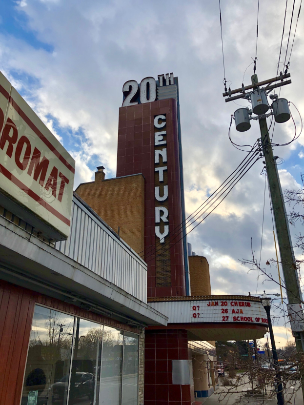 Außenansicht des 20. Jahrhundert-Theaters in Detroit, Michigan, mit Glaswänden, Namensschildern, umgeben von Bäumen und Strommasten mit Drähten unter einem bewölkten Himmel.