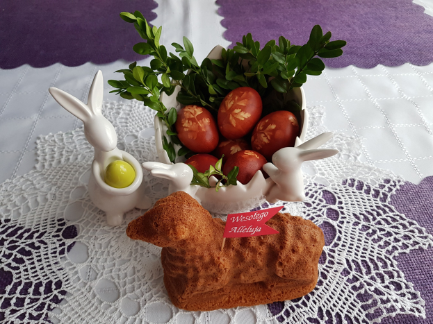 Ein hölzerner Tisch mit einer Decke darauf hält eine Schüssel voller bunter Ostereier mit Bunny-Figuren darauf.