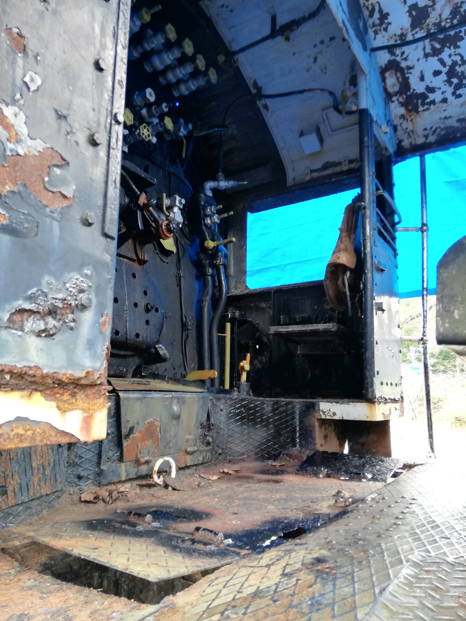 Das Innere eines verrosteten, heruntergekommenen Lkw mit sichtbaren Gebrauchsspuren vor dem Hintergrund von Bäumen und einem klaren blauen Himmel.