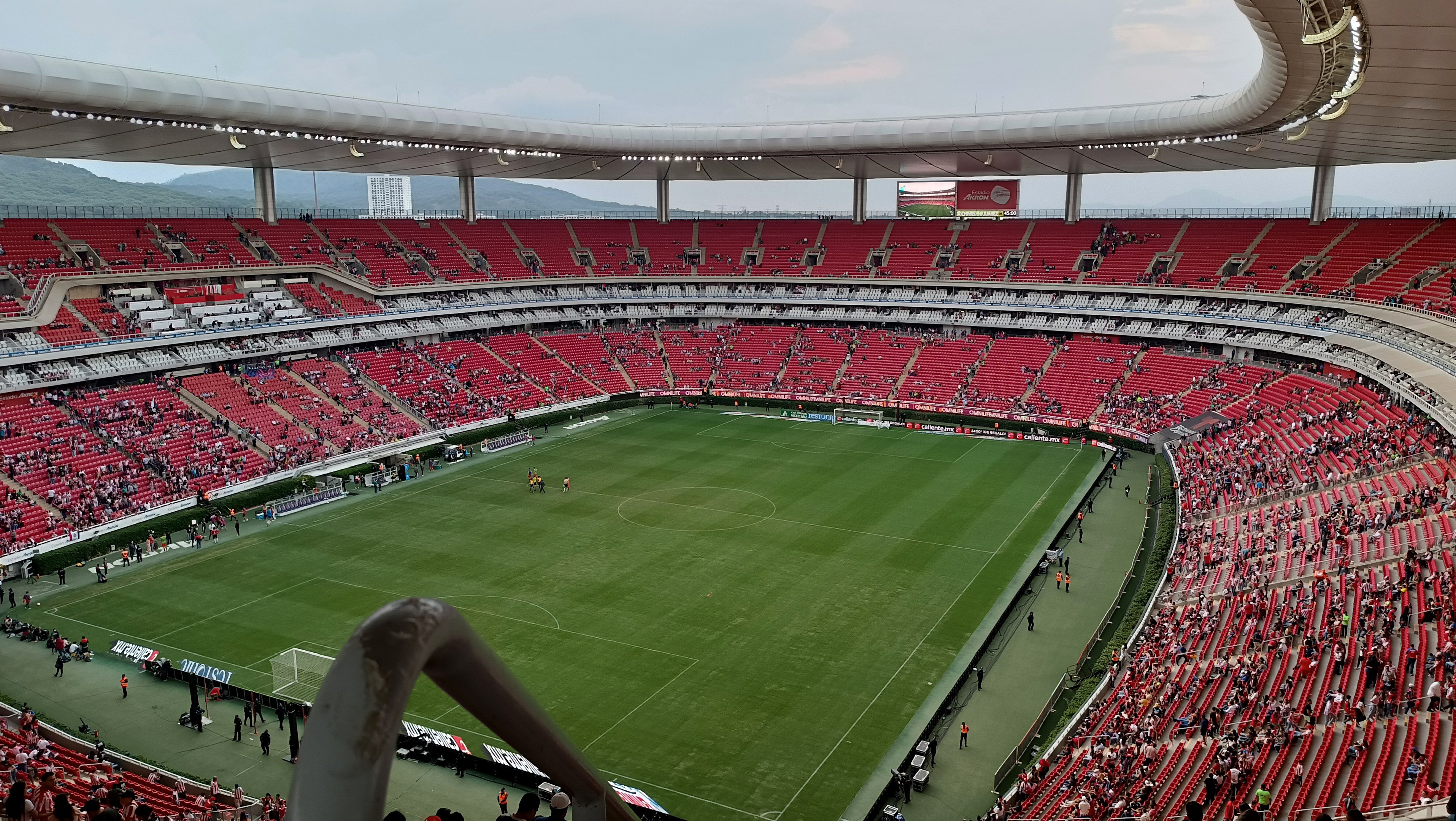 Ein großes Stadion mit Zuschauern bei einem Fußballspiel, Hügel im Hintergrund und ein klarer blauer Himmel.