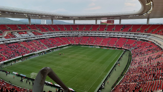 Ein großes Stadion mit Zuschauern bei einem Fußballspiel, Hügel im Hintergrund und ein klarer blauer Himmel.