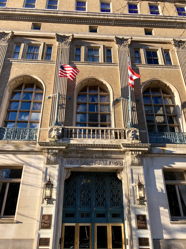 Großes Gebäude mit Glasfront, mehreren Türen, Säulen und Flaggen, als Plaza Hotel in New York City identifiziert.