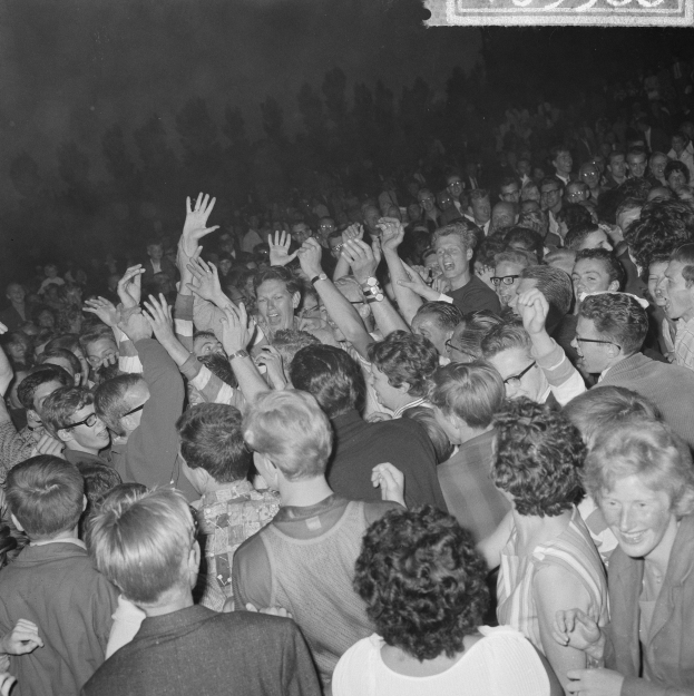 Ein Schwarz-Weiß-Bild einer Menge auf einem Konzert mit erhobenen Händen um ein Schild herum.