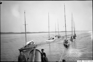 Ein Schwarz-Weiß-Foto von mehreren Segelbooten bei einem Rennen im Wasser mit Menschen an Bord, mit Hügeln und einem klaren Himmel im Hintergrund und einem Text unten, der "Segelbootrennen in San Francisco, Kalifornien" lautet.